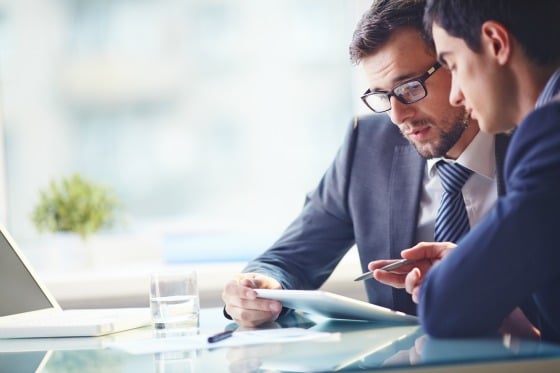 Two men in suits looking over a tablet at a desk