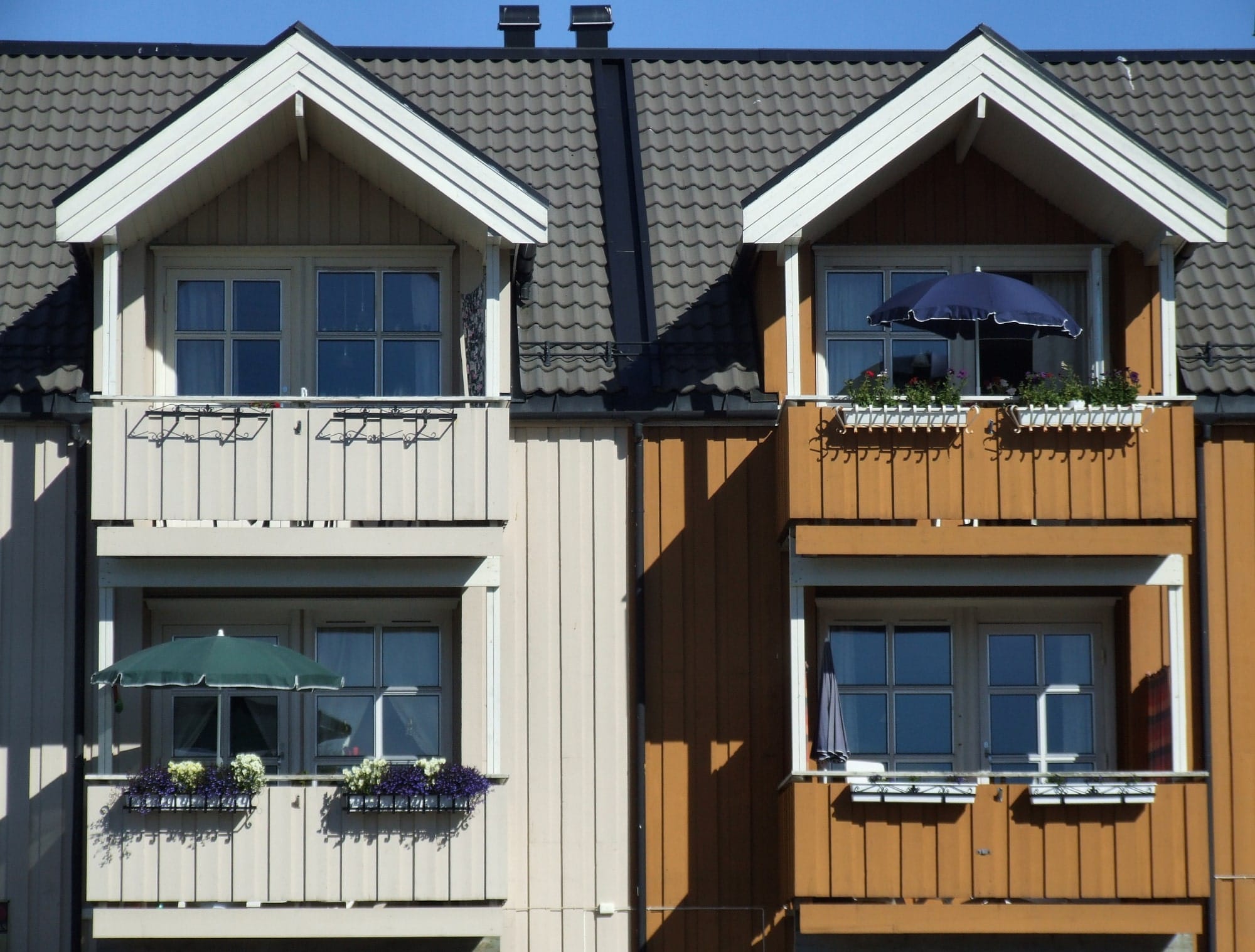 Two adjoining timber-clad houses with balconies, one cream and one brown