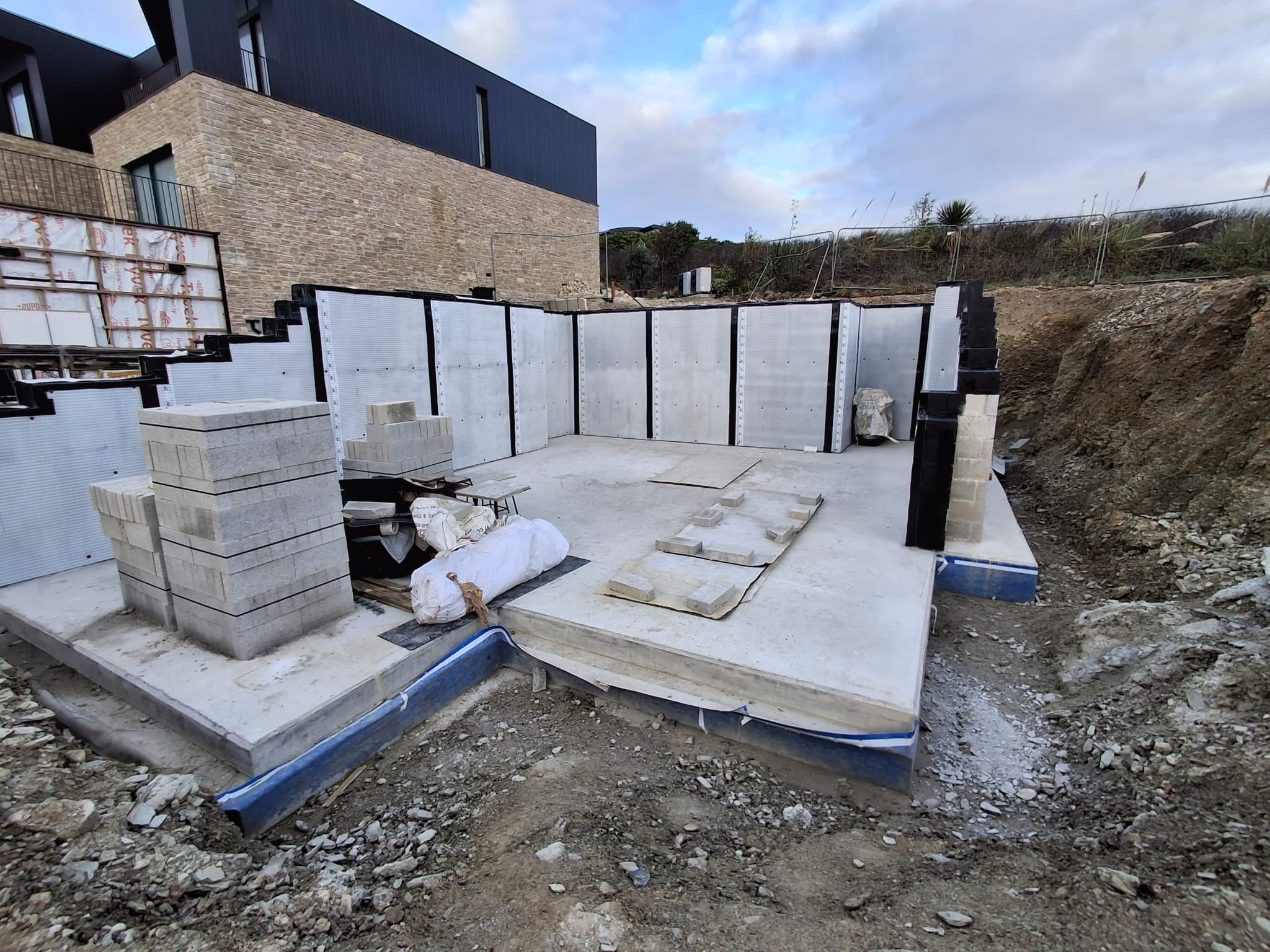 Basement slab and walls lined with white waterproofing membrane beside a brick and black clad house