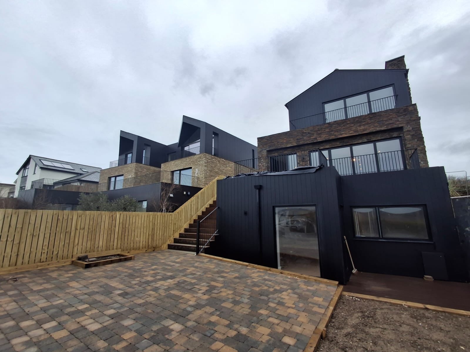 House in dark cladding and stone above a block-paved terrace