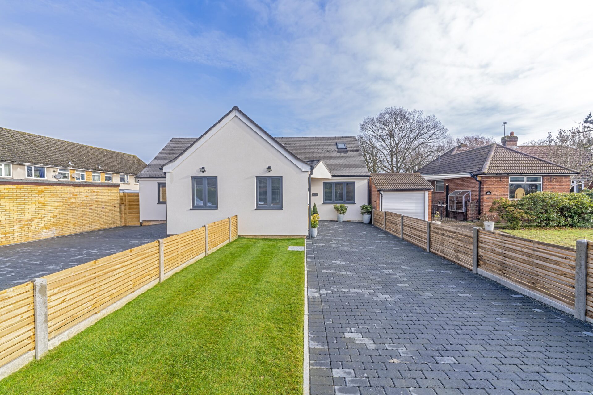 Finished white chalet bungalow with a lawn, fence and block-paved drive