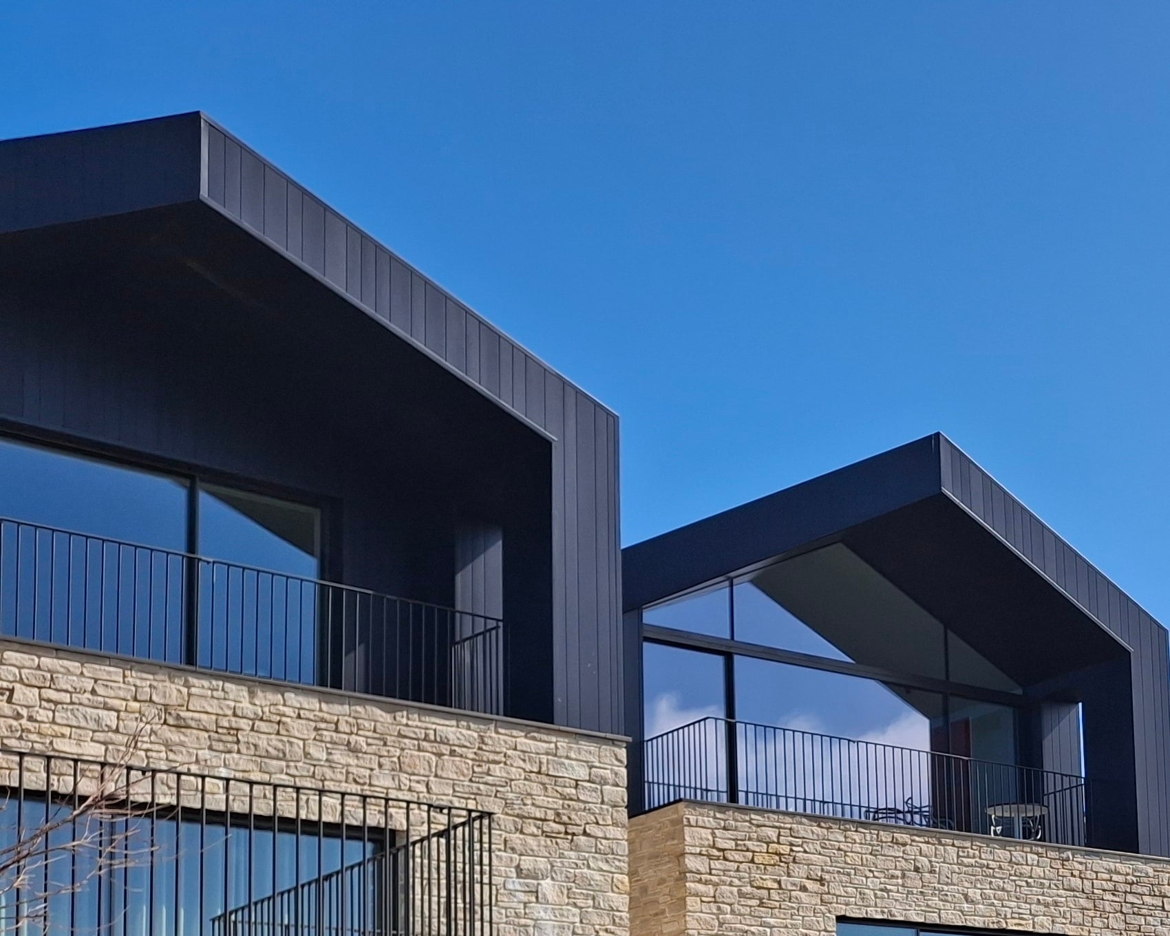 Two finished new homes in dark cladding and stone under a blue sky