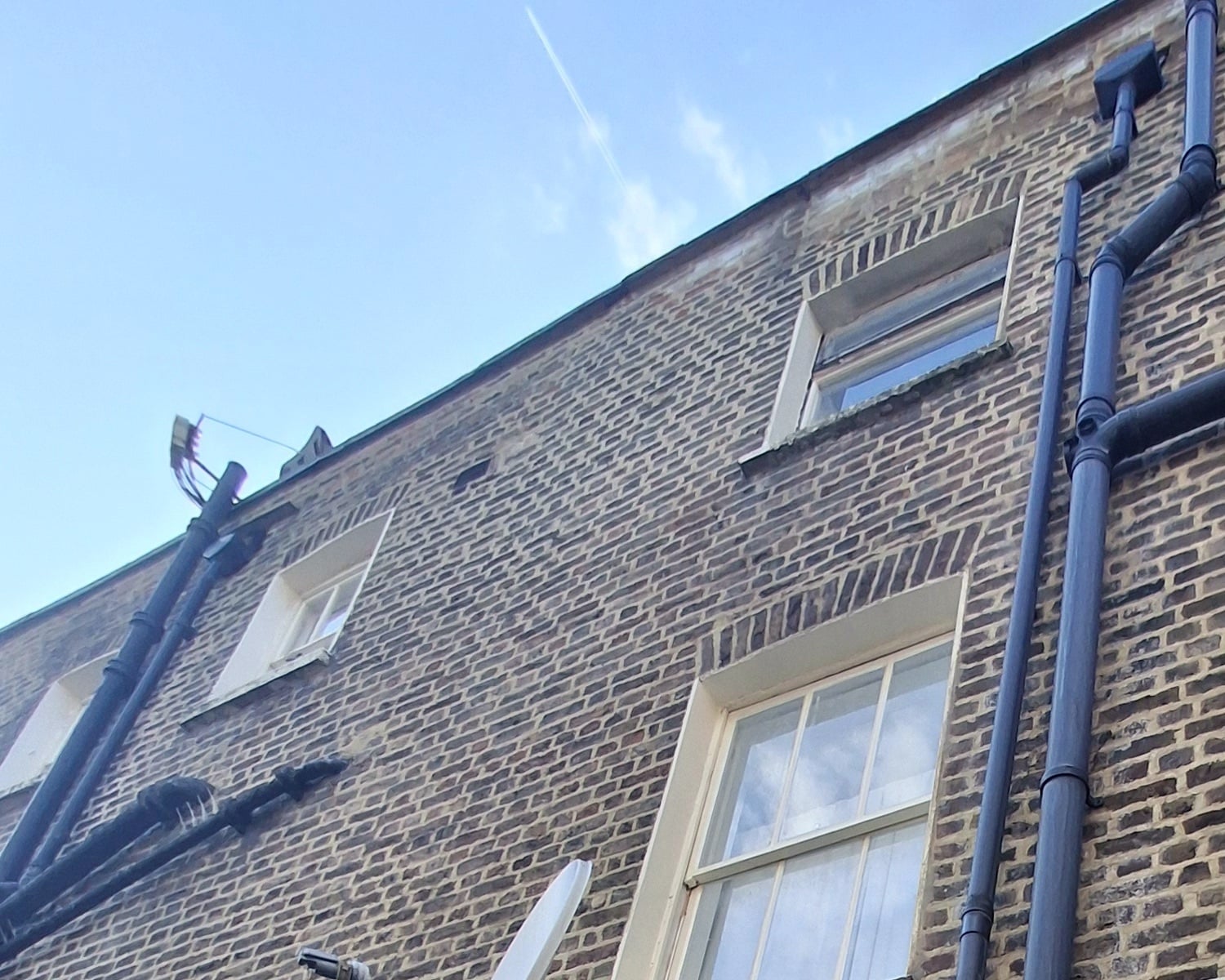 Rear wall of a brick terrace with sash windows and rainwater pipes