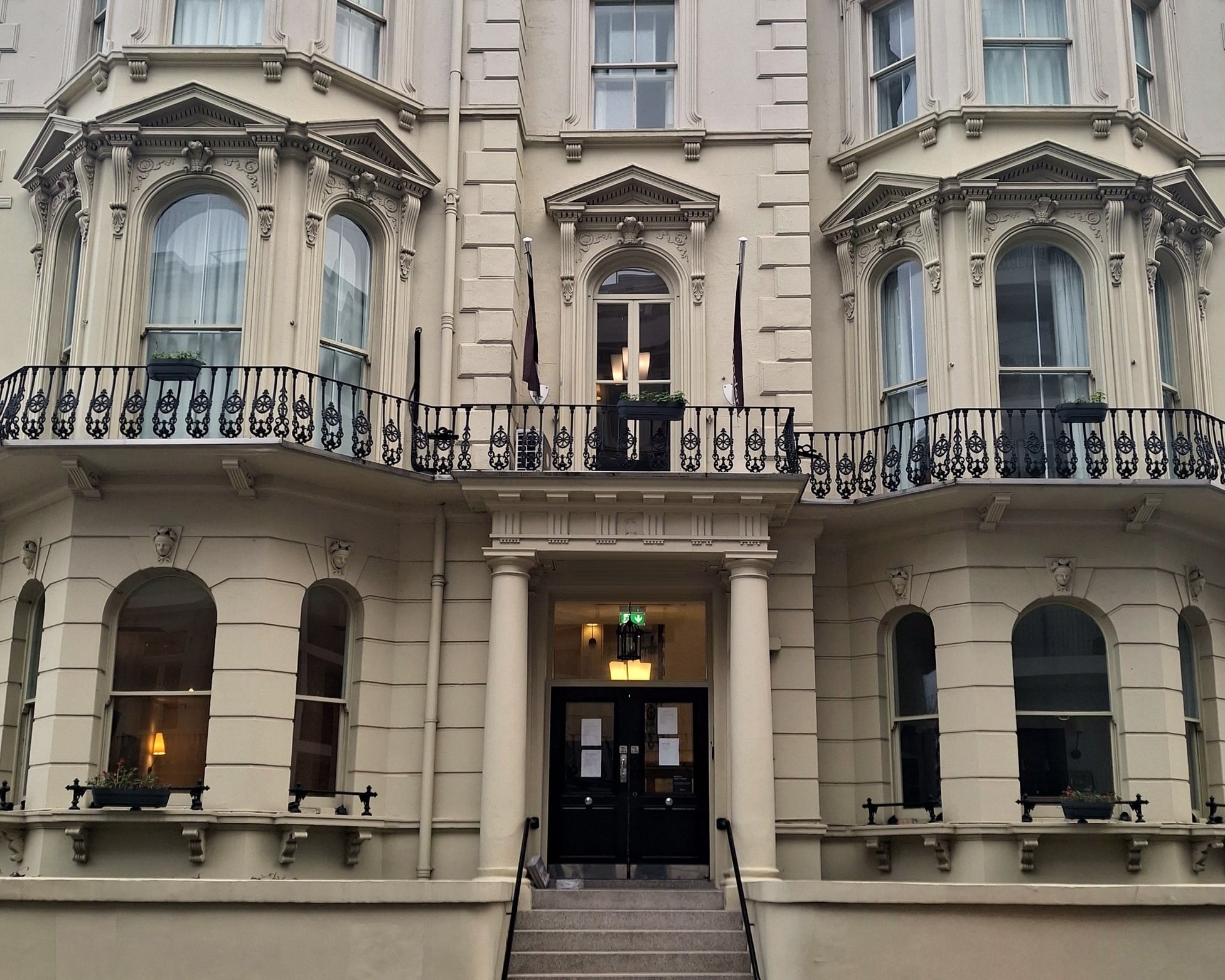 White stucco Victorian building with bay windows and a cast iron balcony above the entrance